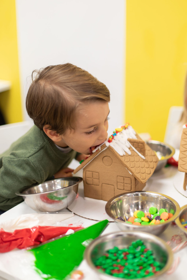 Child taking a bite of his edible decorated gingerbread house at a Sweetology decorating party