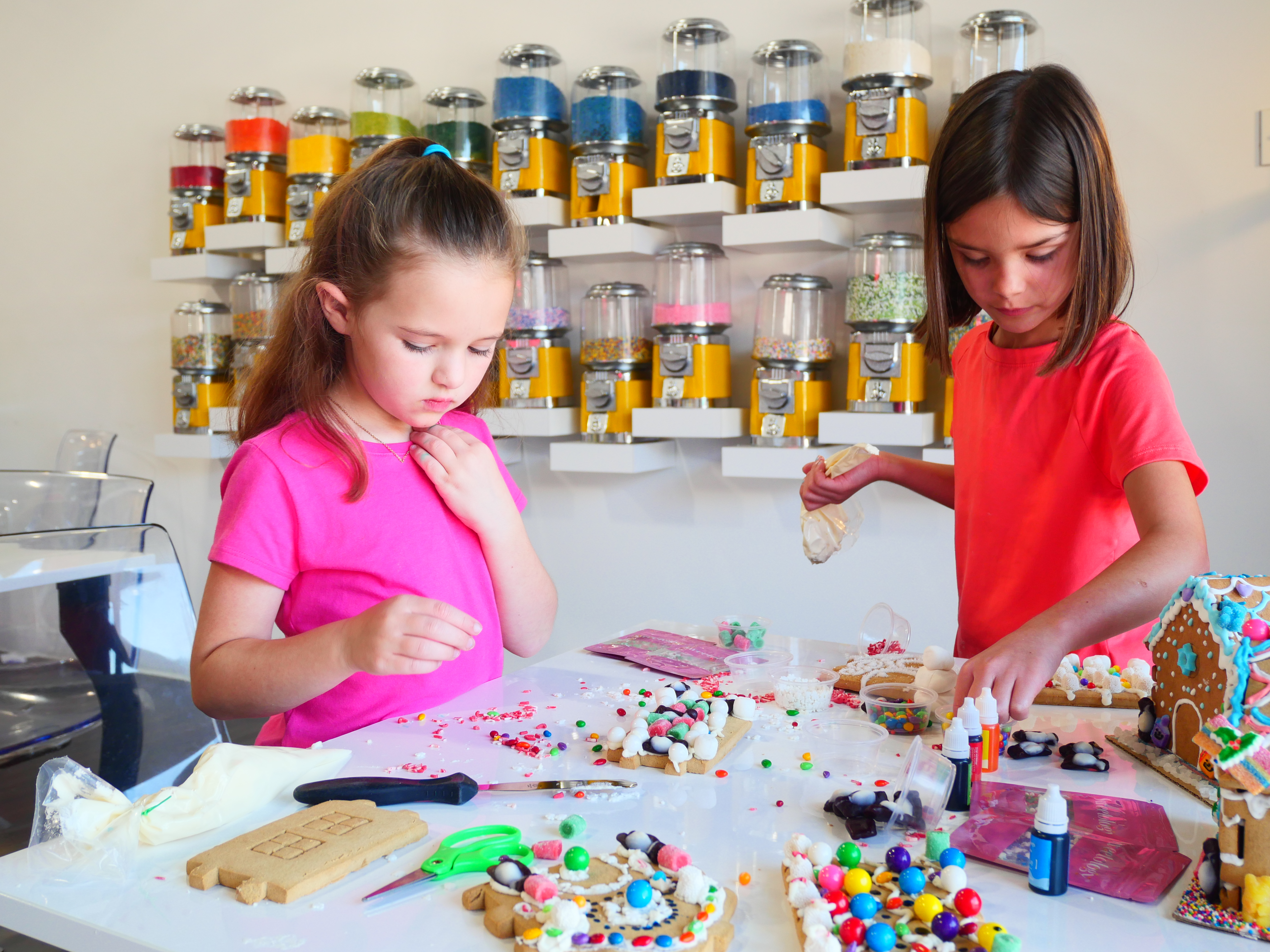 Kids decorating gingerbread houses with candy and icing at the Sweetology studio candy wall — family decorating event
