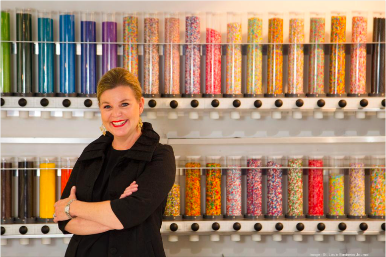 Sweetology founder smiling in front of a colorful wall of sprinkles and candy