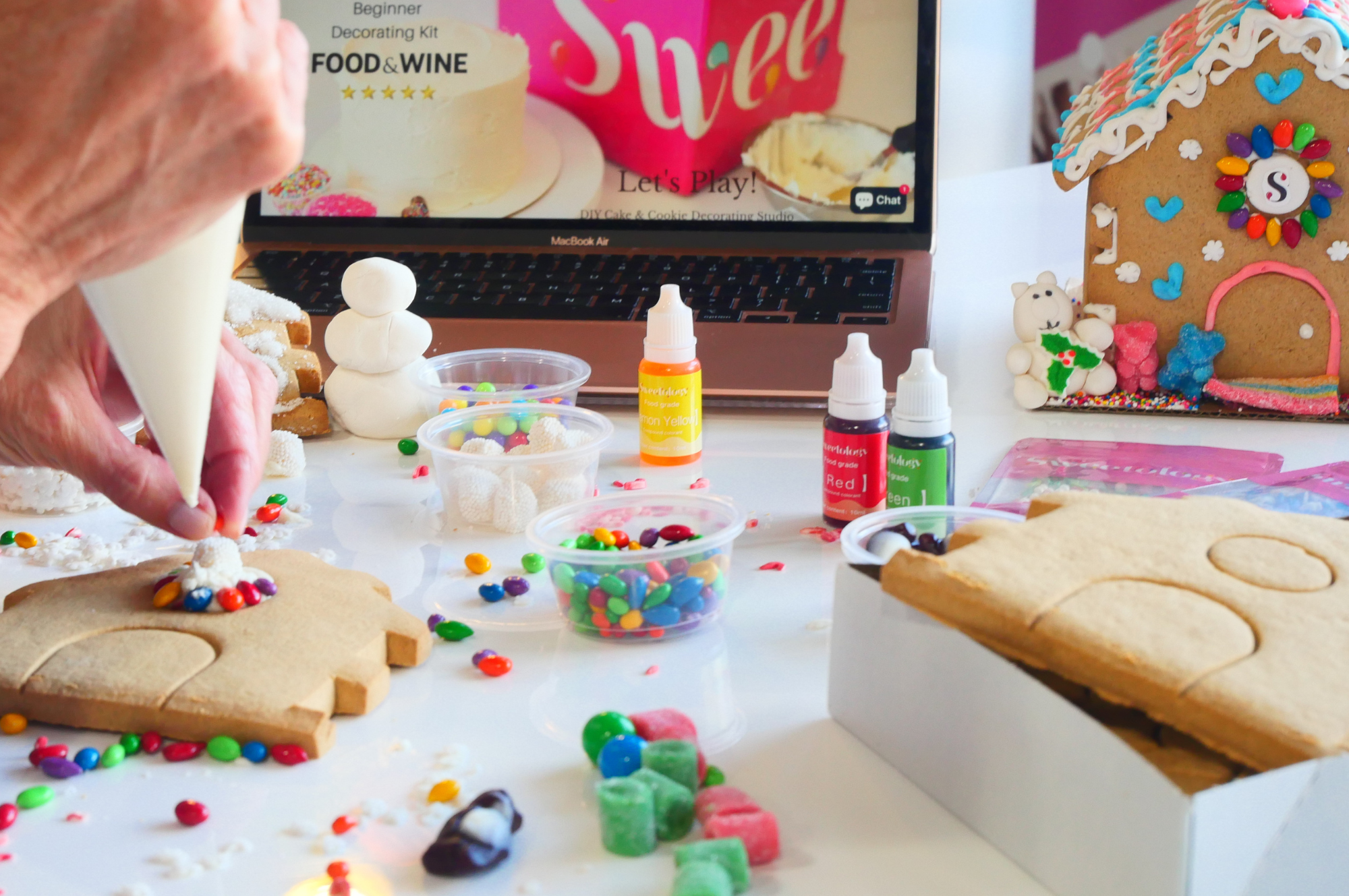 Hands decorating gingerbread with candy and icing on a live virtual Sweetology event